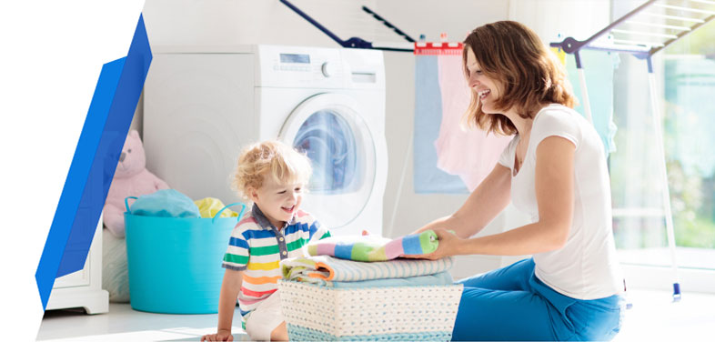 Woman and child sitting on the floor in a laundry room with a tumble dryer, folding clothes together.