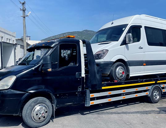 A broken-down taxi minibus is being carried on top of a pickup truck