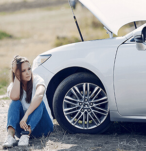 A woman is sitting beside a broken car.