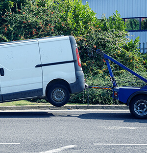 Image of a white broken-down delivery van being carried by a pickup truck
