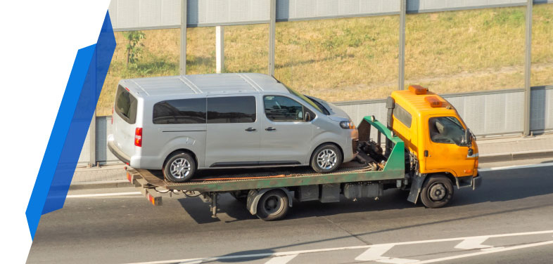 Silver minibus being towed on a yellow flatbed tow truck on a road with smart cover mini bus breakdown insurance cover