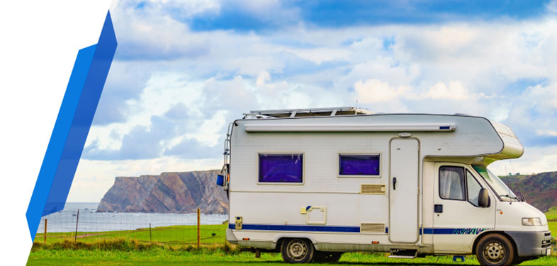 White motorhome parked on a grassy field near a cliff and the sea under a cloudy sky.