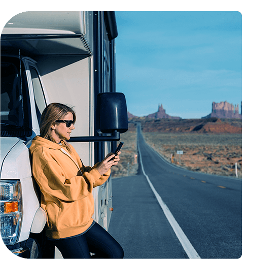 Person standing outside a motorhome holding a phone, parked on a road in a scenic desert area. waiting for smart cover motor home breakdown roadside recovery