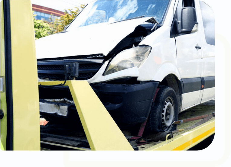 Image of a white taxi minibus with a damaged front side being loaded onto a recovery truck