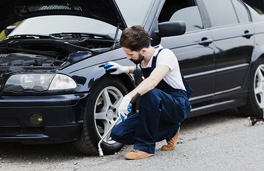 Smart Cover Taxi Minibus Breakdown Cover – Mechanic inspecting the front wheel of a broken-down car on the roadside.