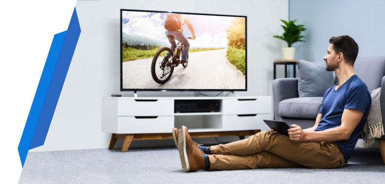 Man watching modern flat-screen TV at home - Smart Cover TV insurance for screen protection and breakdown cover.